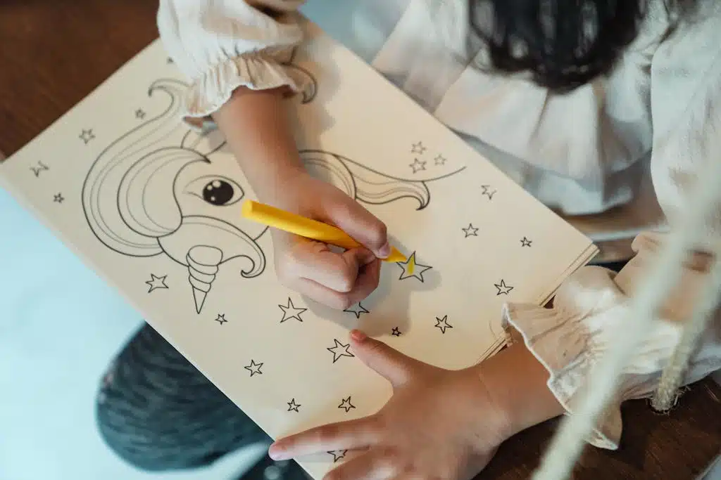A young girl enjoys coloring a unicorn drawing with a yellow crayon in a cozy indoor setting.