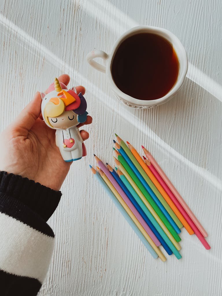 Top view of a toy and coffee cup alongside vibrant pencils on a white table.